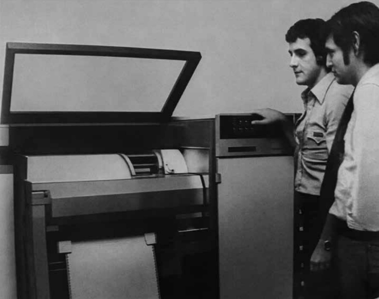 O começo da SIGA, na GEL: dois homens observam um computador e sua impressora de formulário contínuo